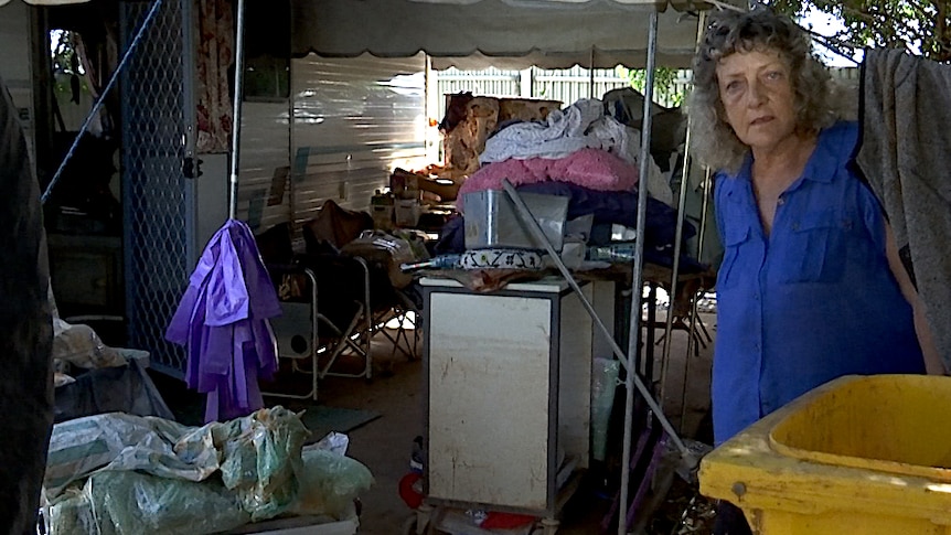 A woman stands outside her caravan with all her flood-damaged property