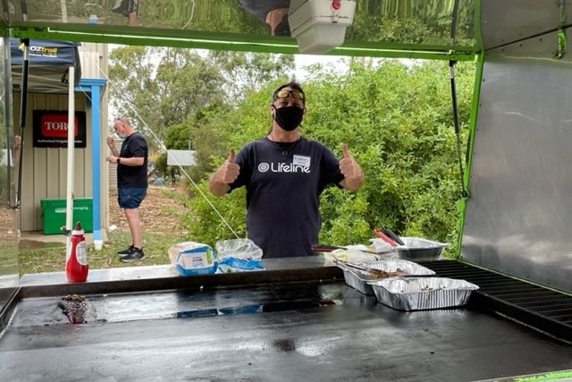 A man stands at a barbecue giving two thumbs up
