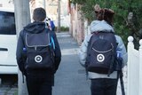 Two unidentified primary school students with backpacks walking down the street.
