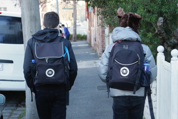 Deux élèves du primaire non identifiés avec des sacs à dos marchant dans la rue.