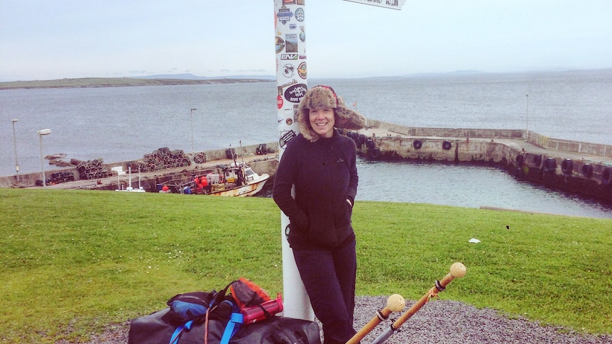 Angela Maxwell stands beneath John O'Groats direction marker 