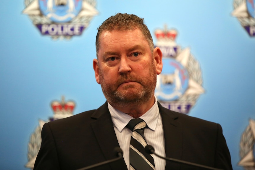 headshot of a man in front of a WA Police insignia backdrop.