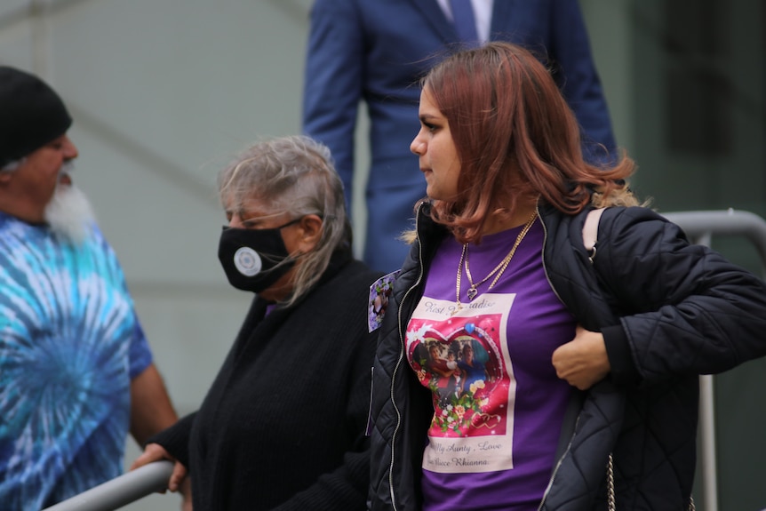 Two Indigenous women, one younger and one older and wearing a face mask, stand side by side outside court.