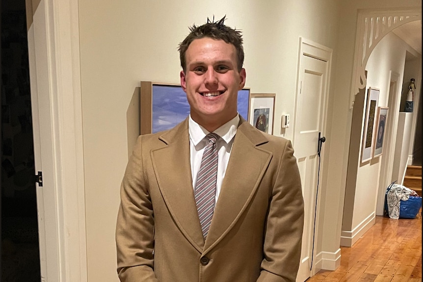 Young man poses smiling in a brown vintage suit.