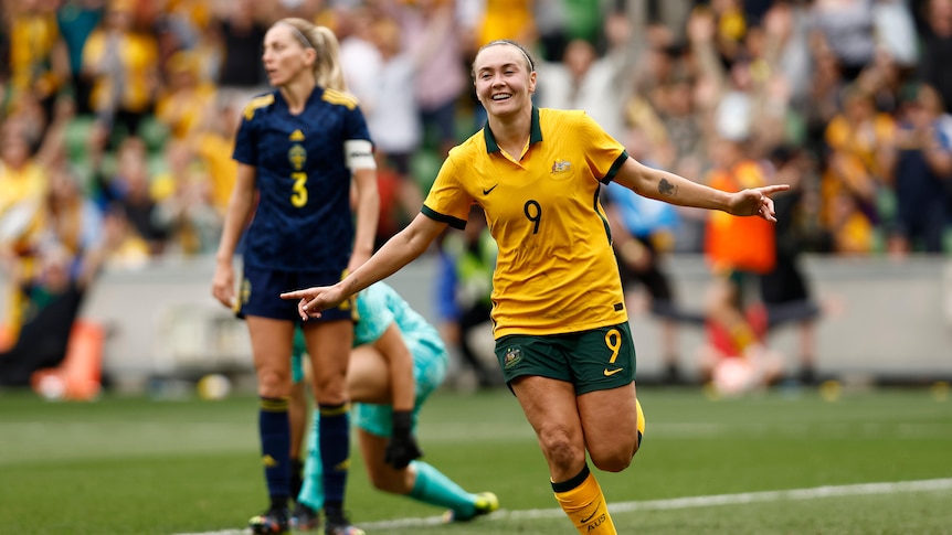 A female soccer player wearing yellow and green smiles after scoring a goal in a game