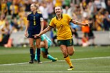 A female soccer player wearing yellow and green smiles after scoring a goal in a game
