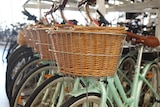 A row of light green bikes with wicker baskets sit in a bike store.