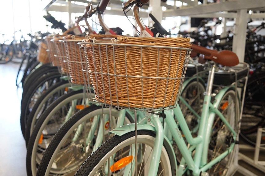 A row of light green bikes with wicker baskets sit in a bike store.