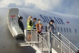 A Silk Air plane on the tarmac in Darwin with students disembarking down steel steps.