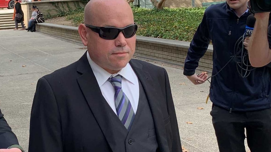 A man in a suit with a bald head and a man in a suit with a tie walk outside a building.