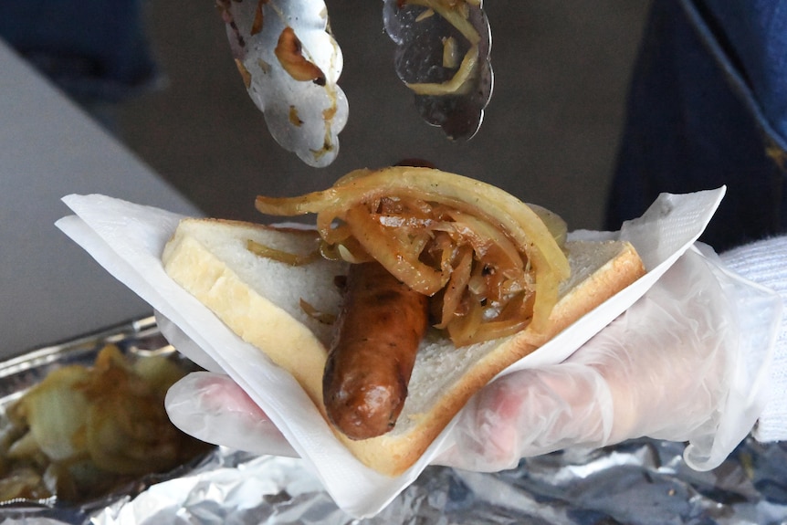 A close shot of a sausage and fried onion being placed on a slice of bread.