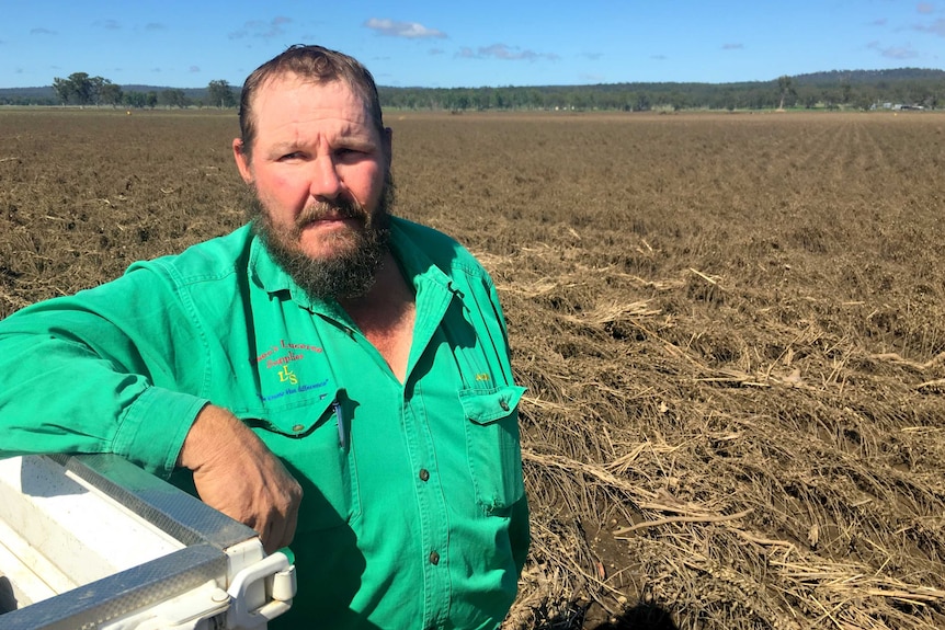 Grain Farmer Jason Larsen leans on his ute with flooded crops in the background