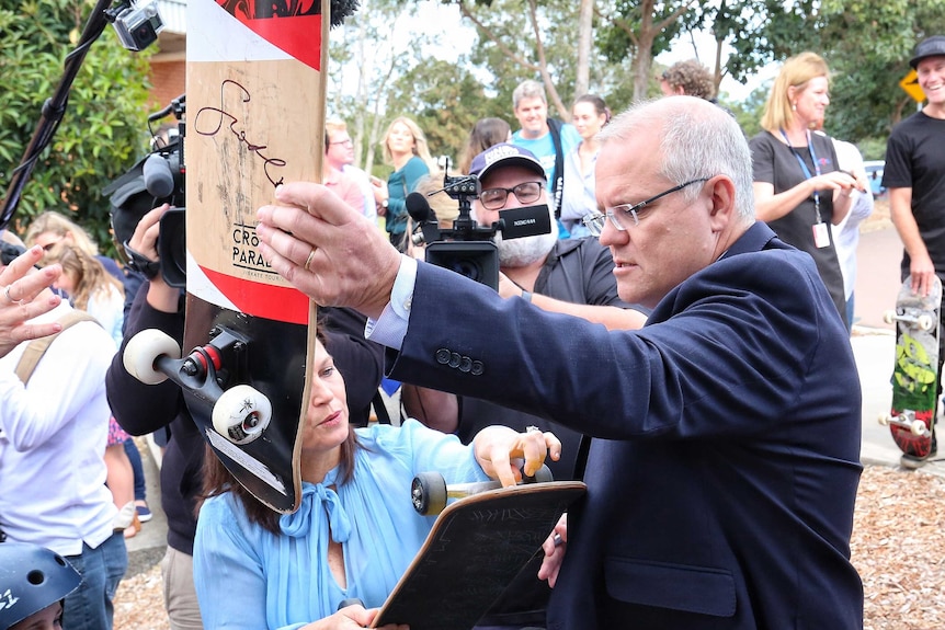 Scott Morrison holds a skateboard up with his signature on the bottom