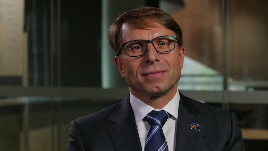 a man with glasses and wearing suit, with a badge showing the ukraine and australian flags on the lapel