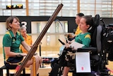 A mother sits in a chair looking across at her daughter who sits in a modified chair as they train for the Paralympics.
