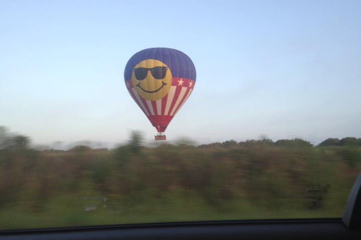 A hot air balloon decorated with a smiley face wearing sunglasses and the colours of the American flag.