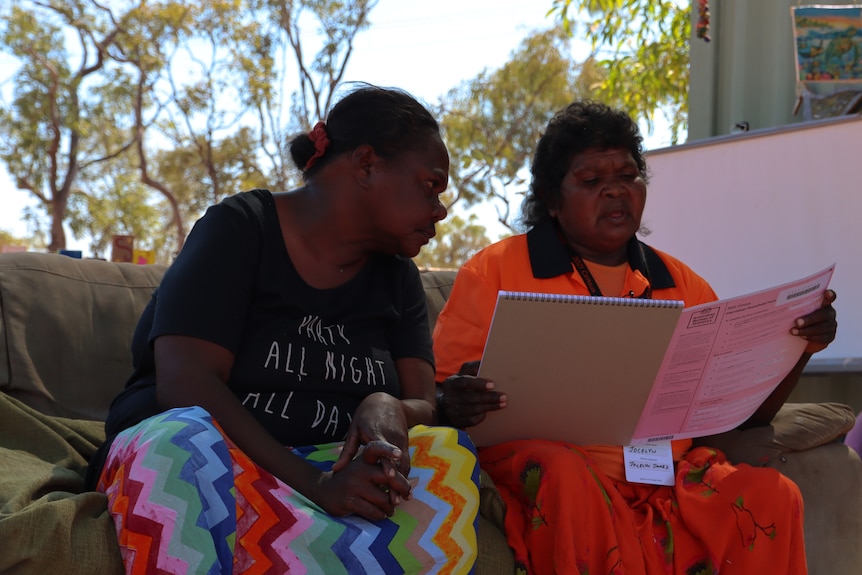 Traditional owner Jocelyn James sits with a woman on a couch assisting her with filling out the Census. 