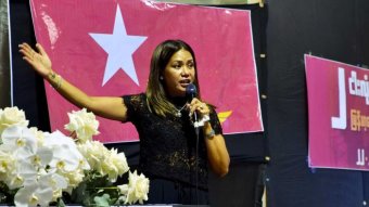 A young woman gestures as she speaks into a microphone.