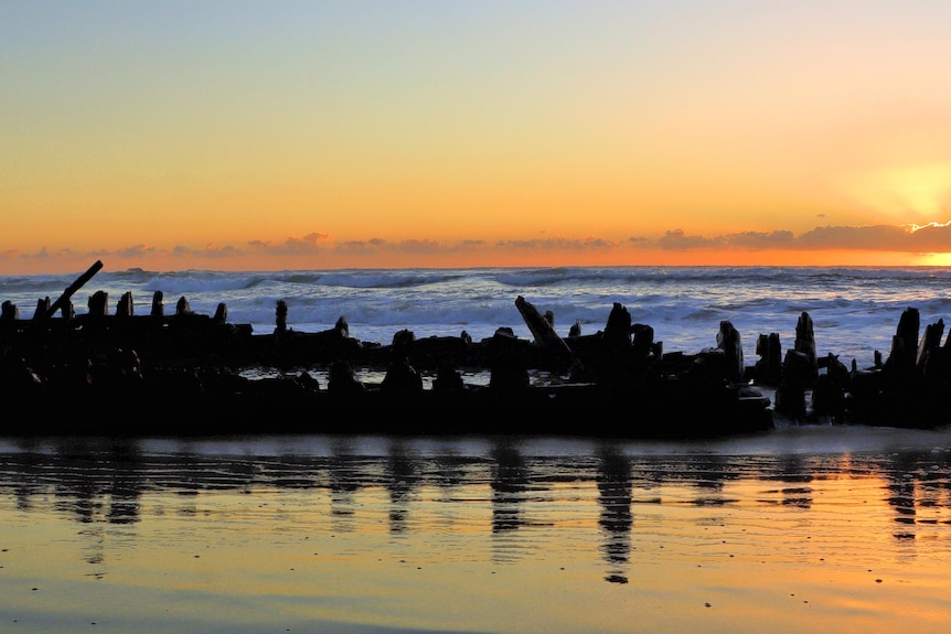 A shipwreck on a beach at sunrise.
