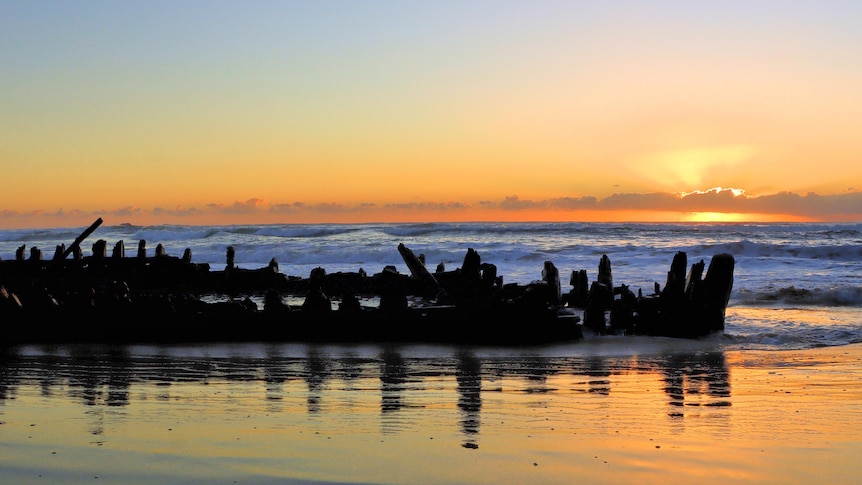 A shipwreck on a beach at sunrise.