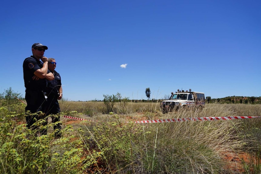 Two police officers stand in scrubland.