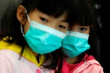 Two young girls with dark hair wear bright blue face masks.