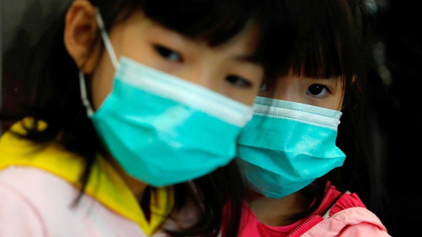 Two young girls with dark hair wear bright blue face masks.