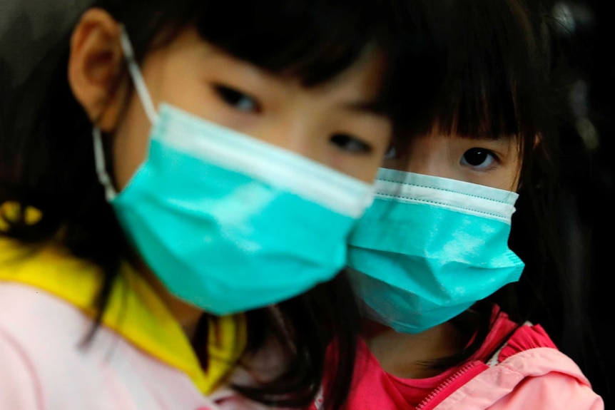 Two young girls with dark hair wear bright blue face masks.