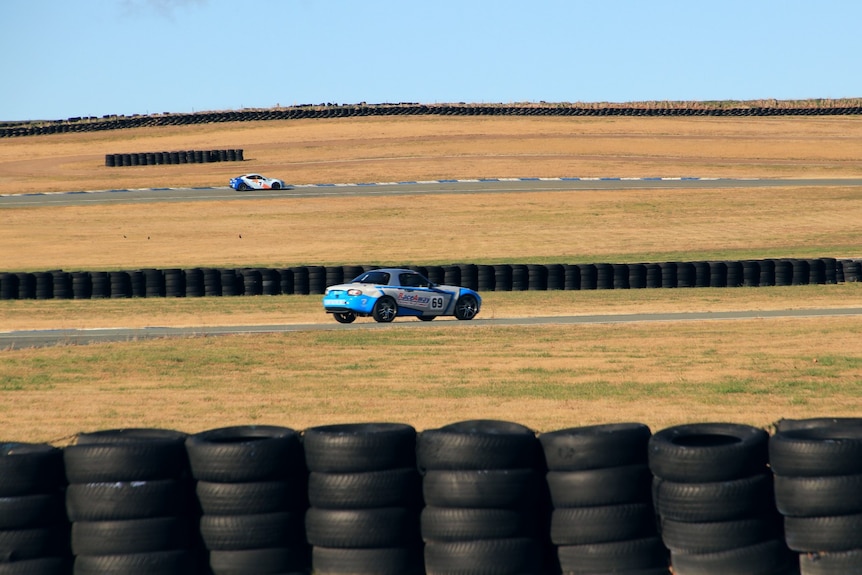 Two cars racing on a track around yellow grass fields.