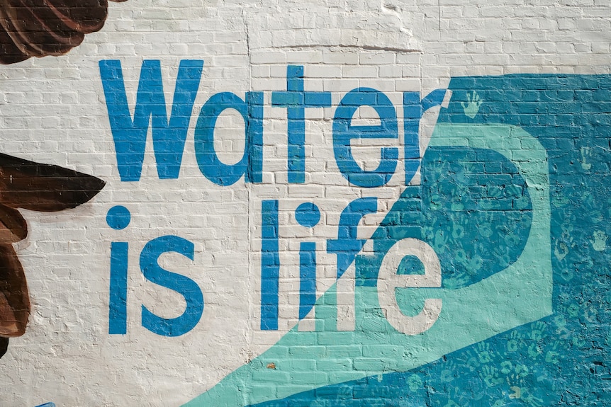 A mural on the side of a brick building that reads 'water is life'.
