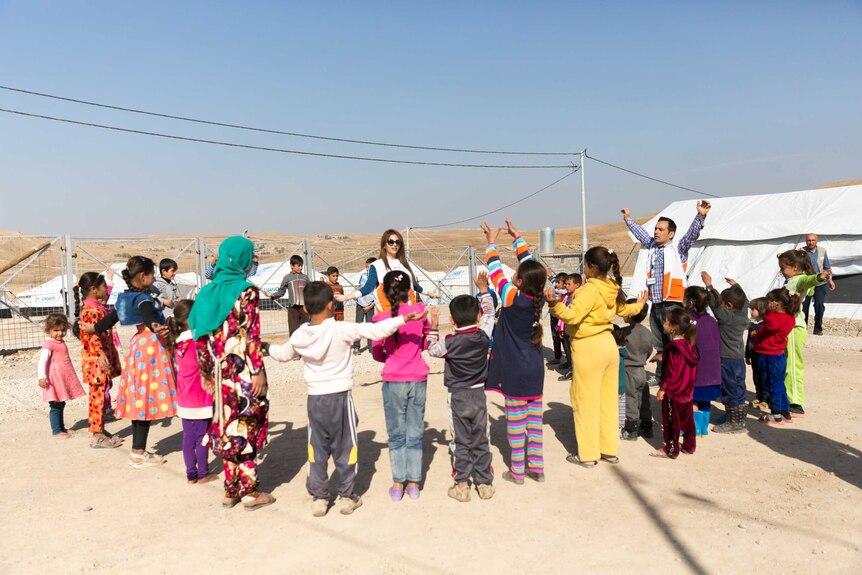 A group of happy children standing in a circle playing a game at Zelican camp outside of Mosul.