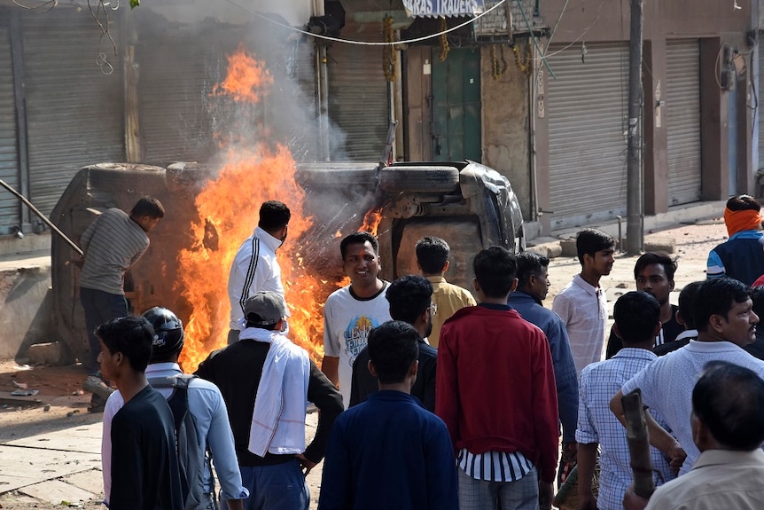 People vandalise and burn a car on the streets of New Delhi.