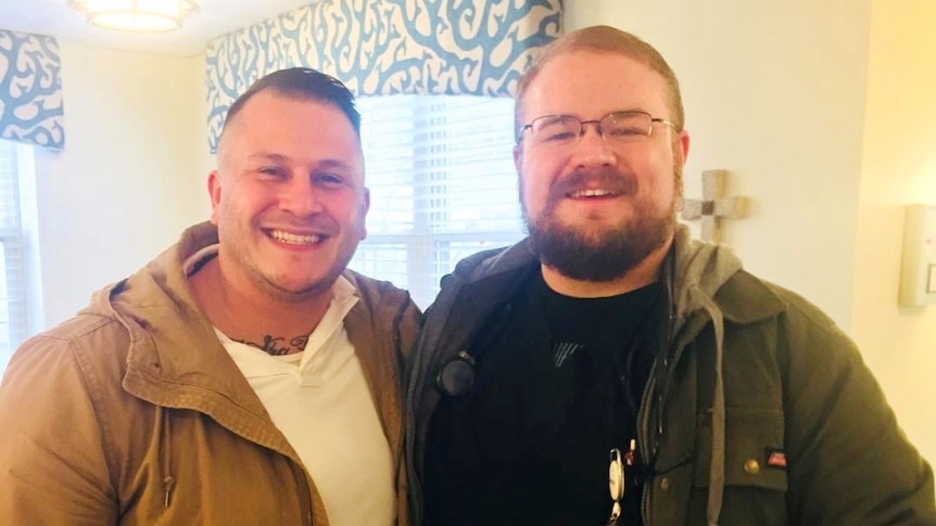 Josh Gregory wearing casual clothing and a nurse's badge, smiling at the camera. 