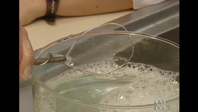 Hand holds wire loop above soapy liquid, bubble surface stretches across wire loop