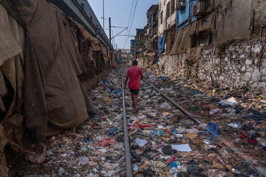 A man walks on a railway track littered with plastic and other waste materials.