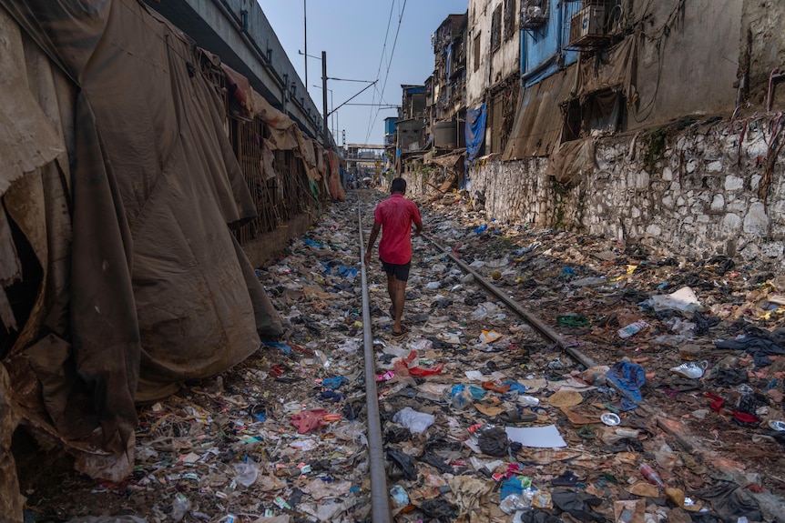 A man walks on a railway track littered with plastic and other waste materials.
