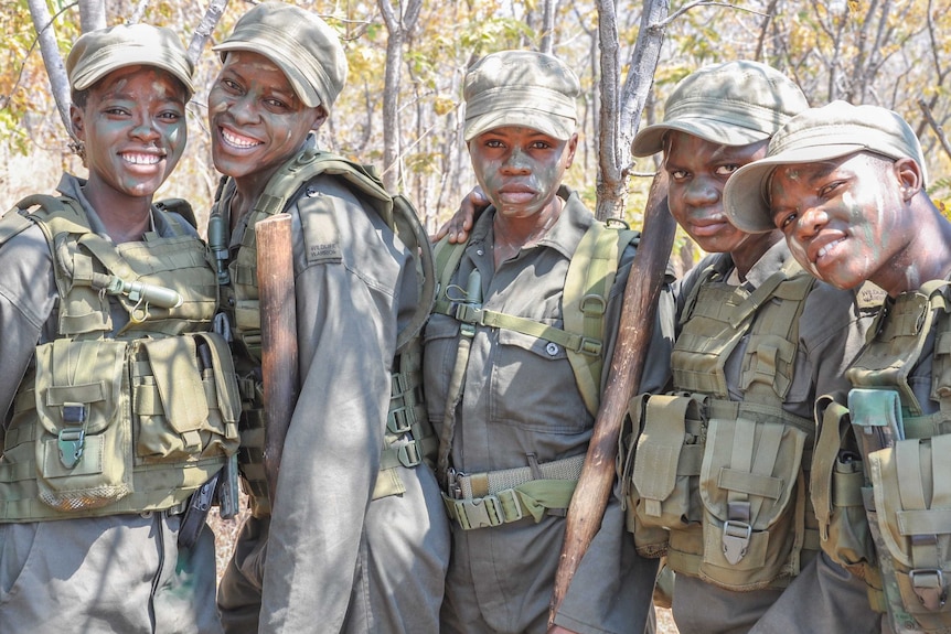 Five Akashinga women looking to camera, wearing camouflage, green hats and and green face paint.