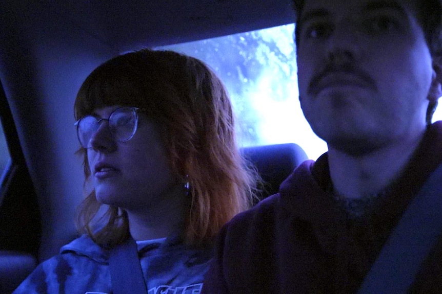 A young woman with red hair and glasses in a car with a young man
