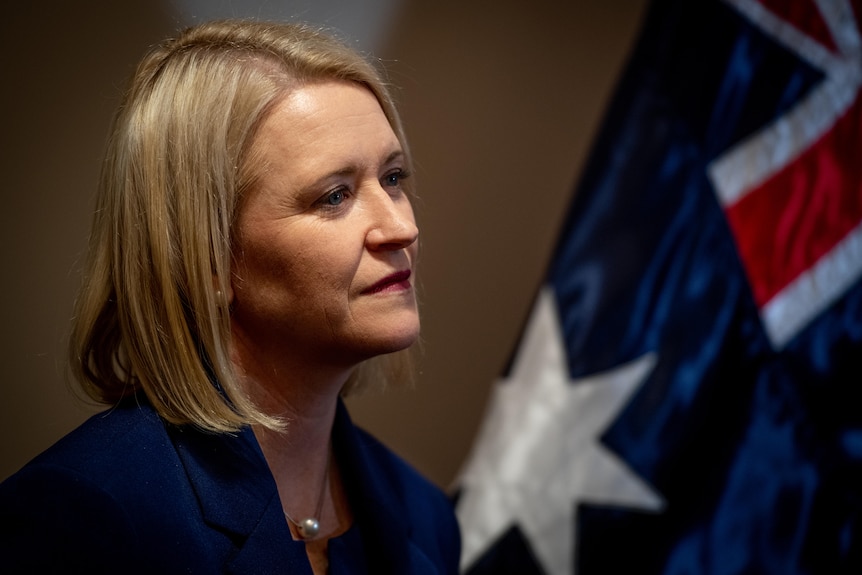 a blonde woman standing in front of an australian flag