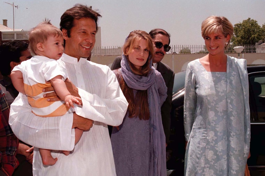 Imran Khan holds a baby boy while standing next to Jemima wearing purple and Princess Diana in a blue floral dress