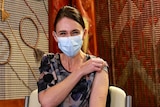 Ms Ardern holds her sleeve up to her shoulder. Her eyes squint and you can tell she is smiling under her surgical mask