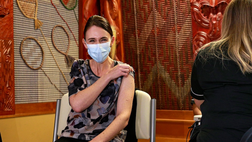 Ms Ardern holds her sleeve up to her shoulder. Her eyes squint and you can tell she is smiling under her surgical mask