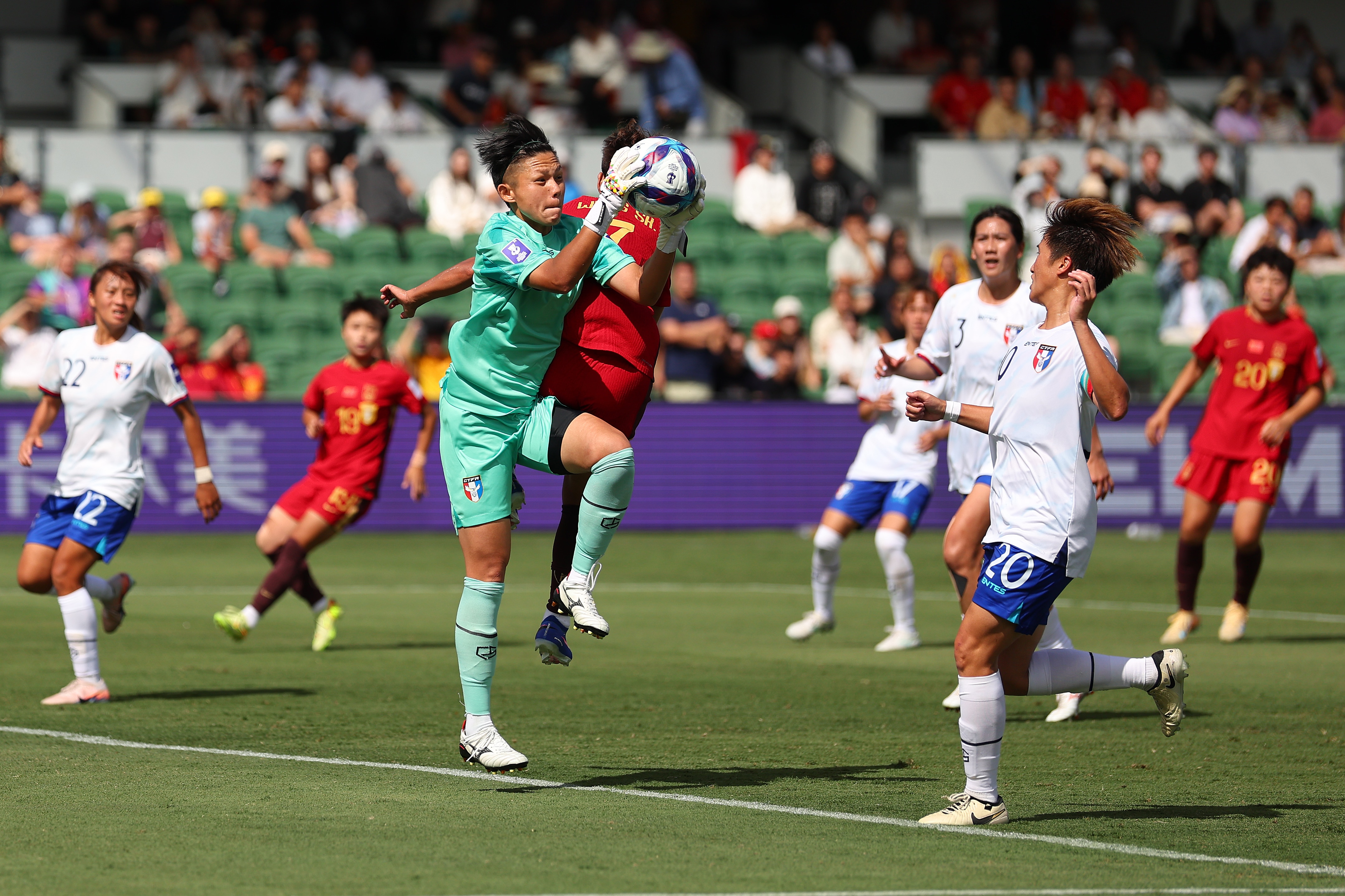 A goalkeeper in green catches a ball amongst players in red and white