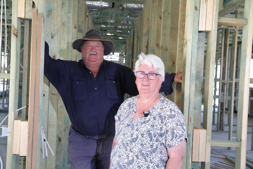 A man and a woman stand in a house frame. 