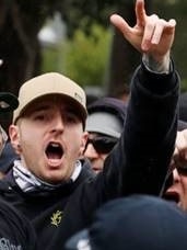 A young man with a beige cap stands in a crowd and shouts, raising his hands.