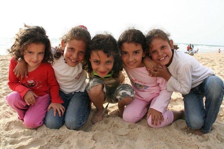 A medium photo of a group of five young girls kneeling and huddling in a line on a beach