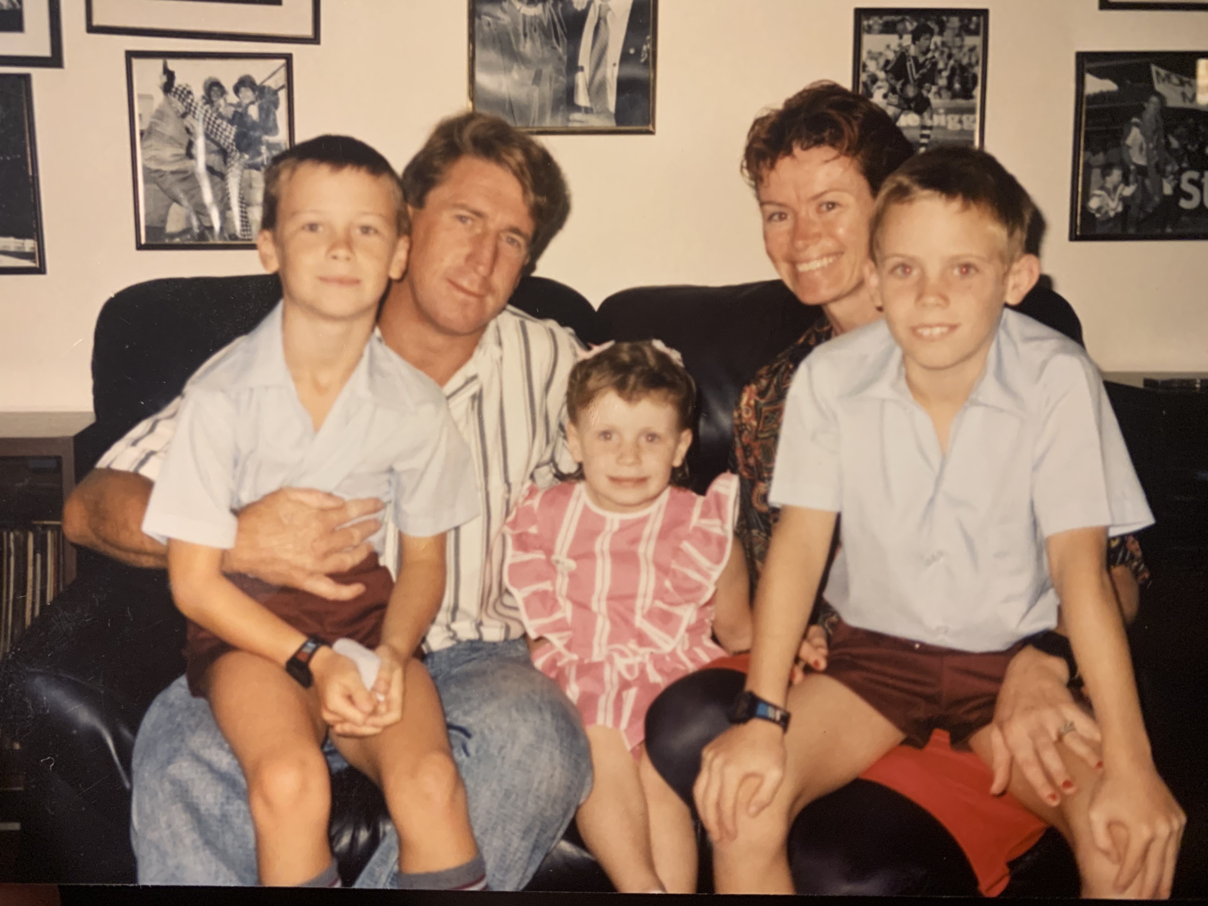 Erin with her mum, dad and brothers as young kids, sitting on a couch with two boys in parents' laps and girl in the middle.