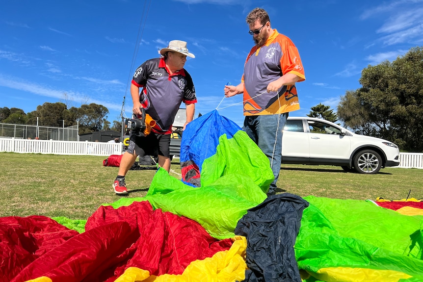Two men stand with a huge amount of colourful light weight fabric on the ground