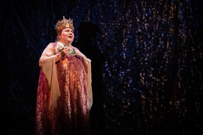 Grace King in a pink and gold gown singing in front of a sparkling curtain backdrop.