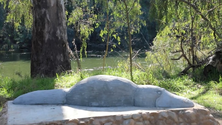 a sculpture of a platypus sits beside a river